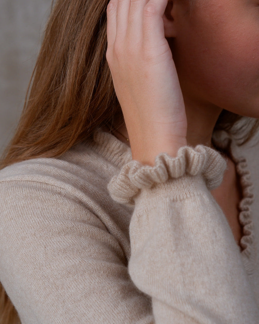 Model iført cashmere bluse i Natural Sand med flæsedetaljer ved halsudskæring.