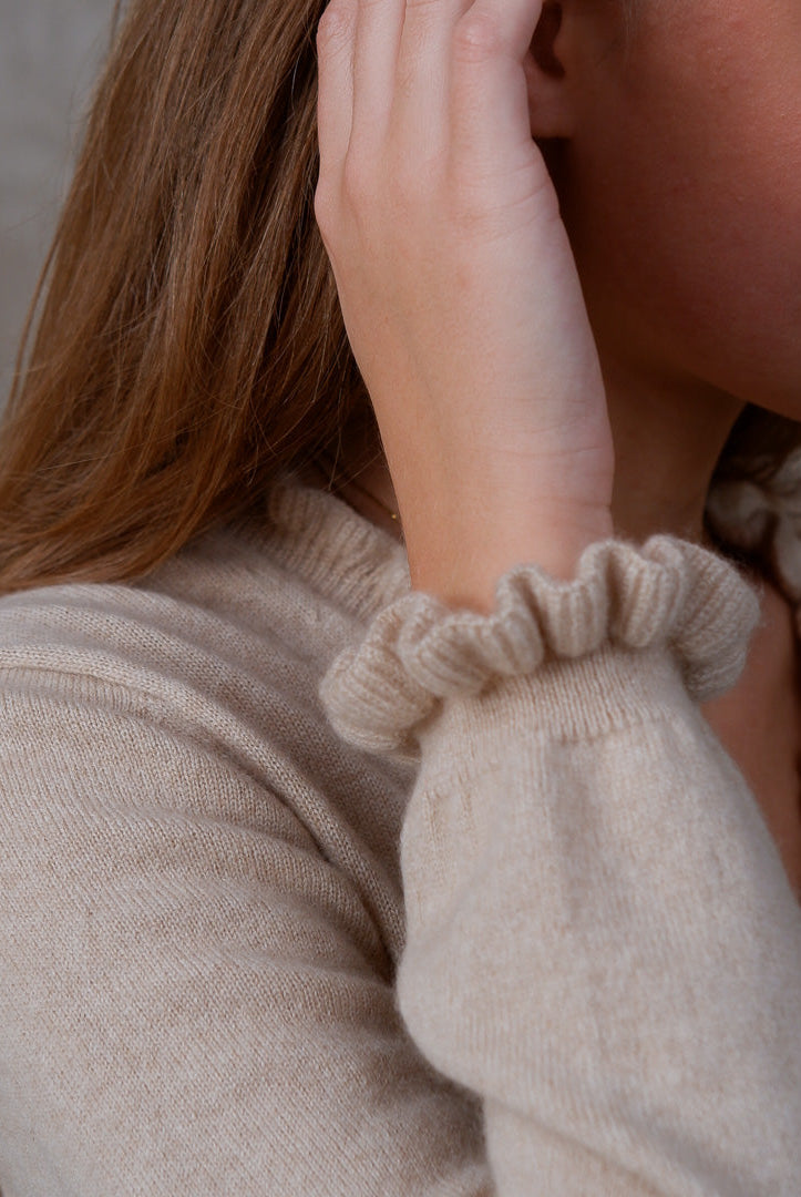 Model iført cashmere bluse i Natural Sand med flæsedetaljer ved halsudskæring.
