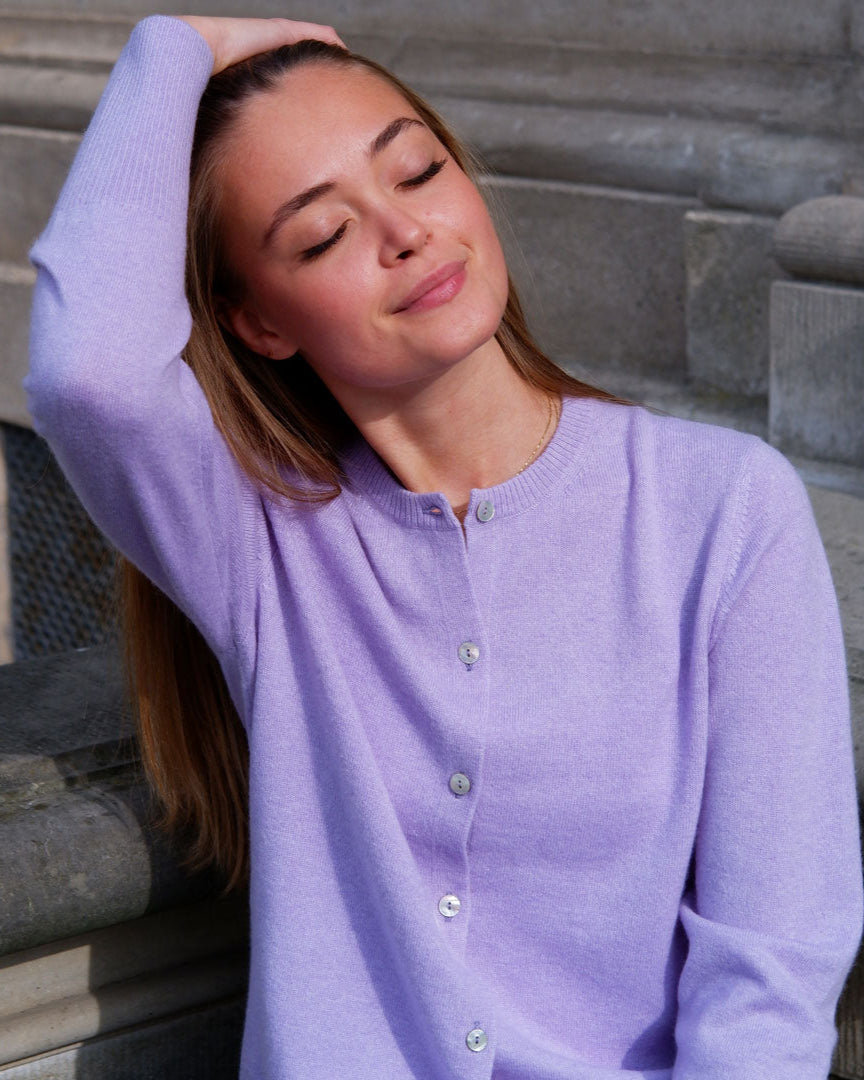 Kvinde iført en lavendelfarvet cashmere cardigan med knapper, sidder afslappet med hånden i håret.