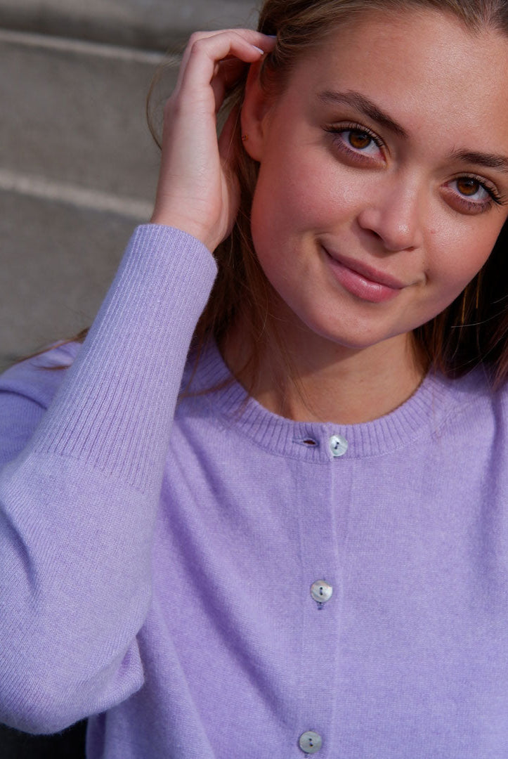 Smilende kvinde iført lavendel cashmere cardigan med knapper, sidder på en trappe.