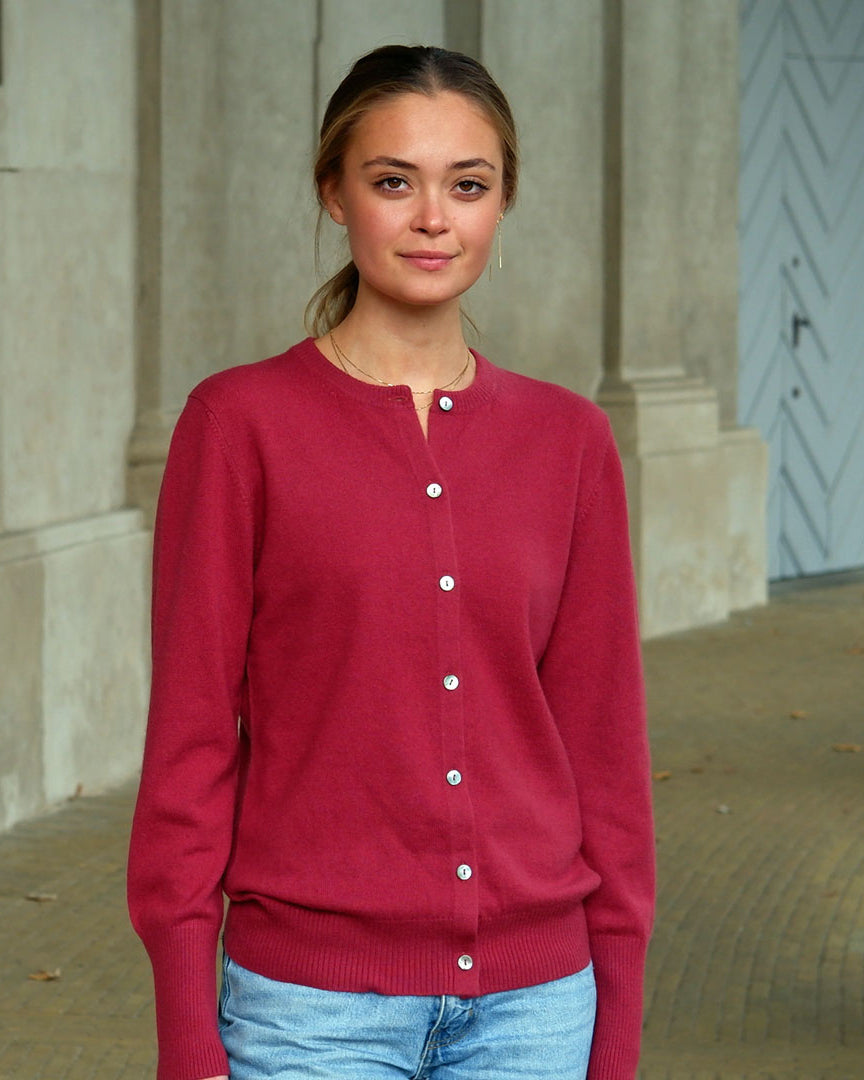 Kvinde iført en Pinot Red cashmere cardigan med knapper, står foran en søjlegang.