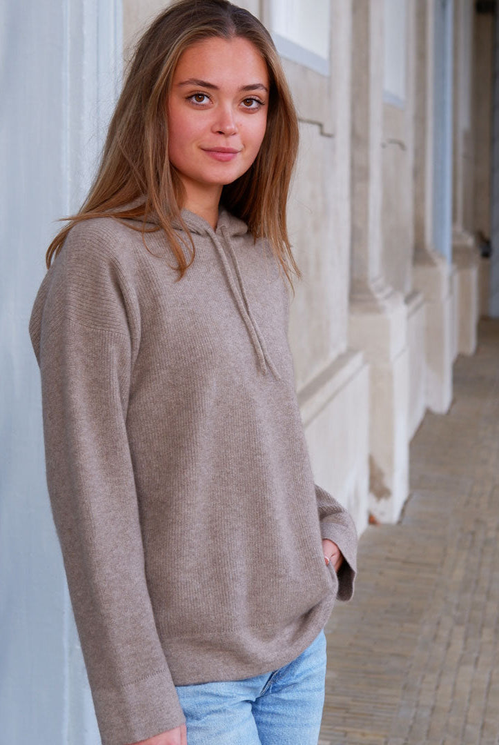 Model i taupe beige cashmere hoodie foran klassisk bygning