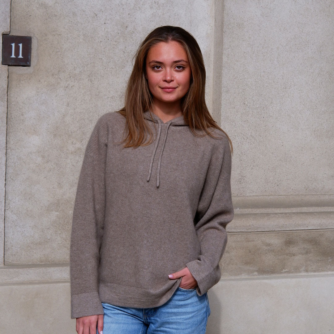 Model i taupe beige cashmere hoodie foran sandfarvet væg
