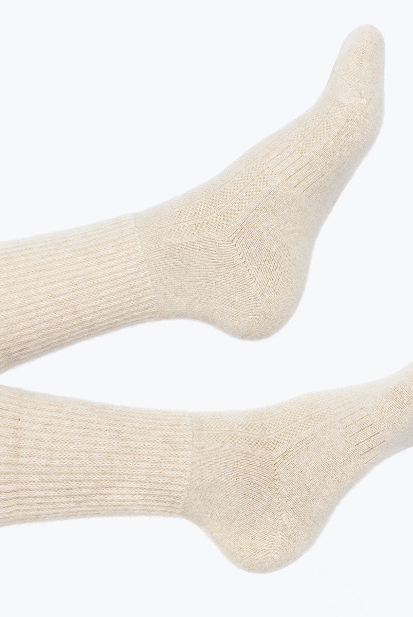 Model iført lys beige cashmere sokker fra Undarmaa, afslappet i et hyggeligt miljø.