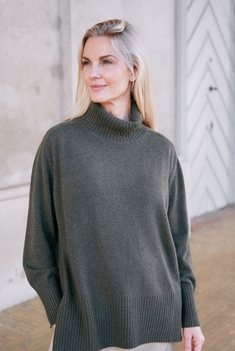 Model iført klassisk cashmere sweater med sadelskuldre og løs pasform i army green i afslappet pose.
