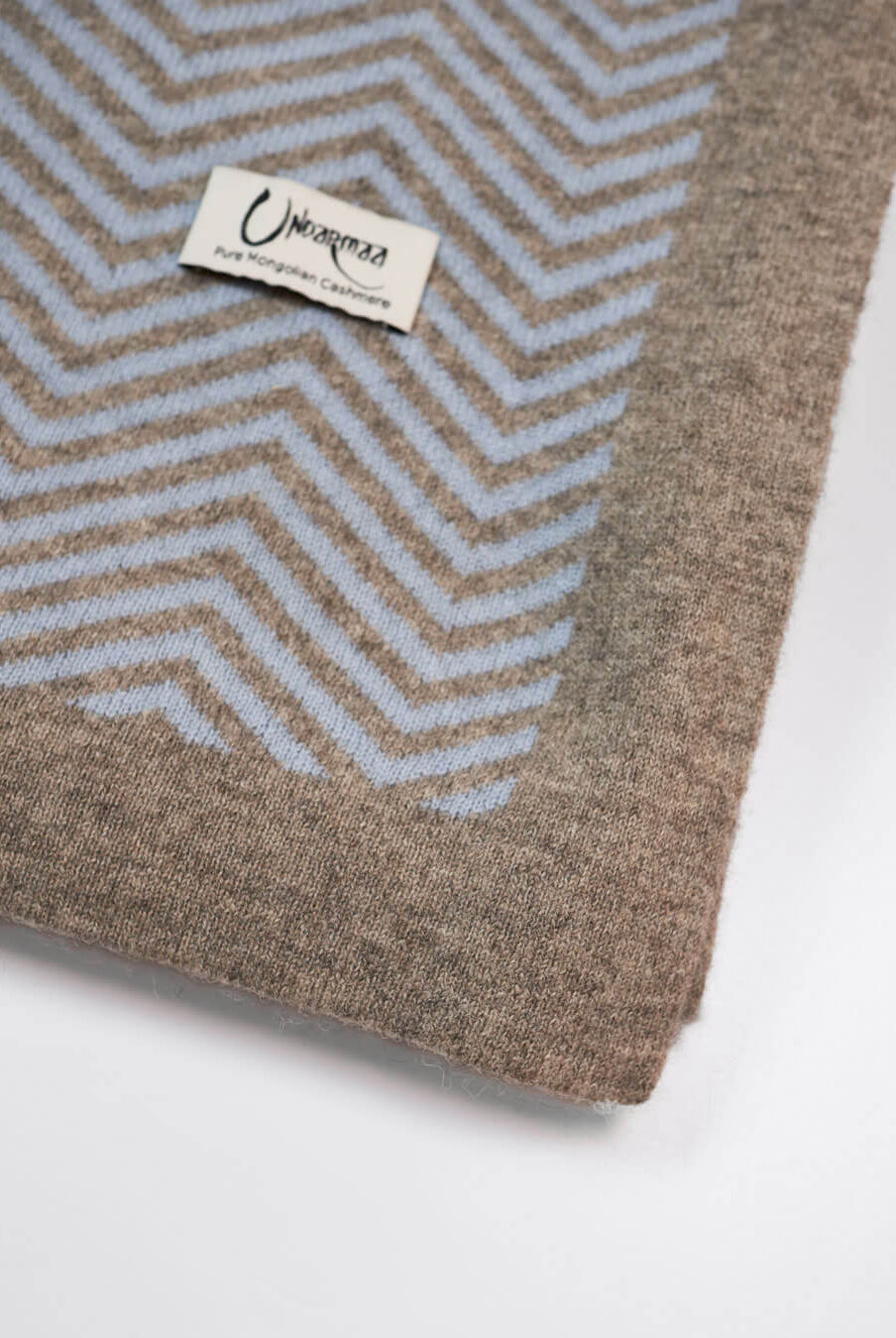 Detalje af plaid i ice blue cashmere og platinum grey yakuld med Undarmaa-logo, i sildemønstret design.
