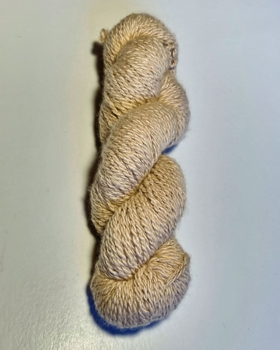 Håndspundet cashmeregarn i natural sand på bord.