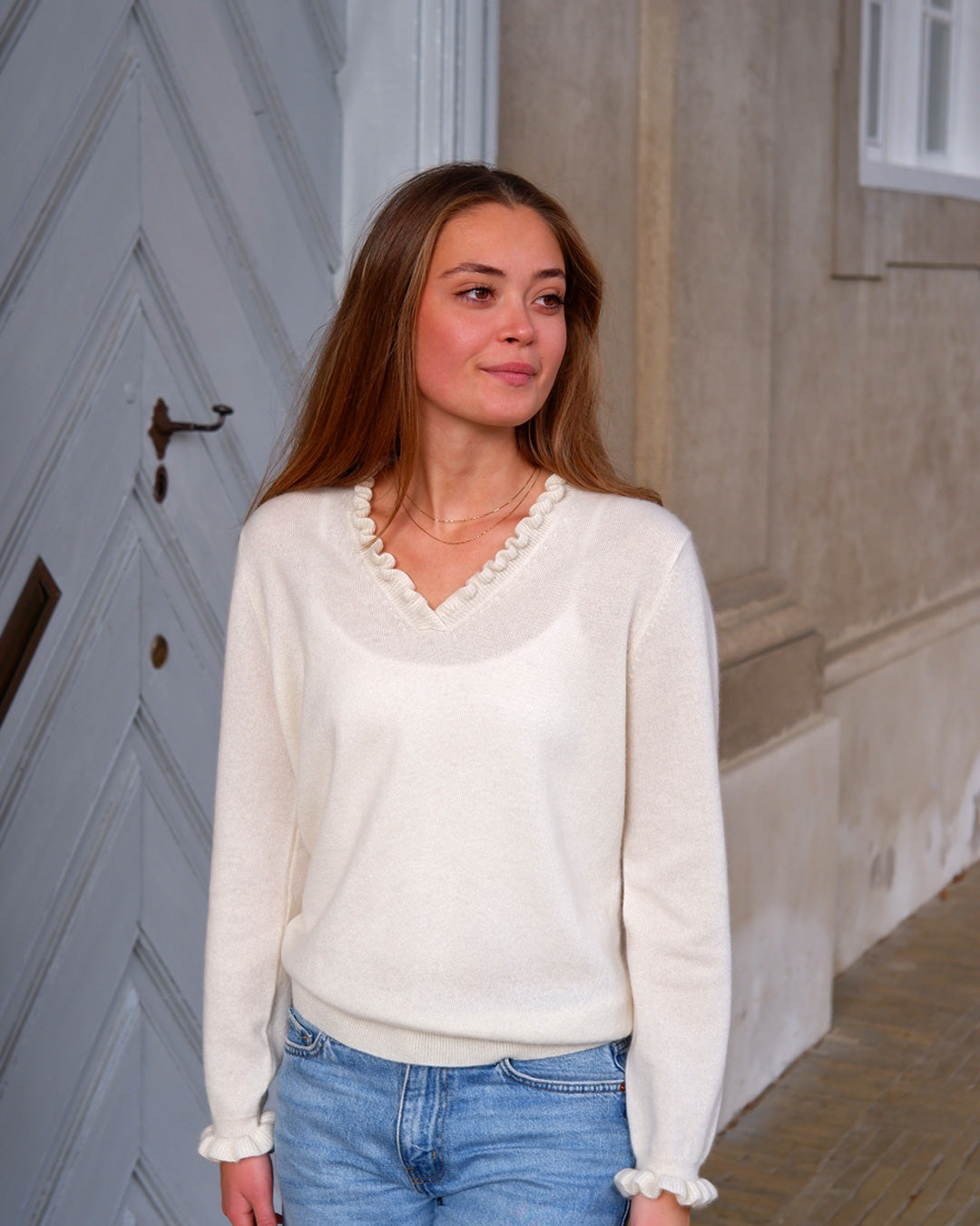 Kvinde iført cashmere bluse i Natural white med flæsedetaljer ved halsudskæring.