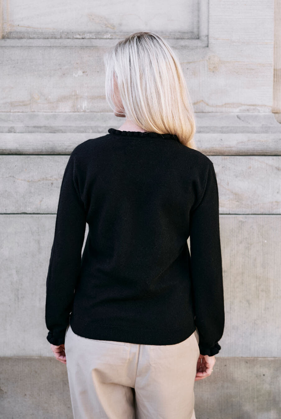 Kvinde iført cashmere bluse i Black med flæsedetaljer ved halsudskæring, set bagfra.