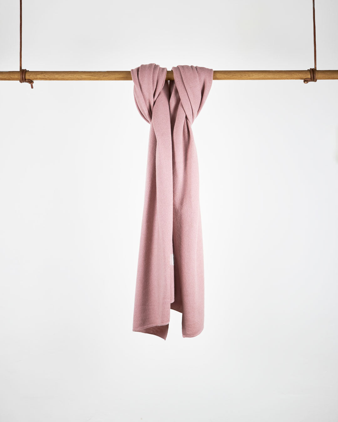 Tørklæde i cashmere, dusty pink, hængende på stang mod hvid baggrund.