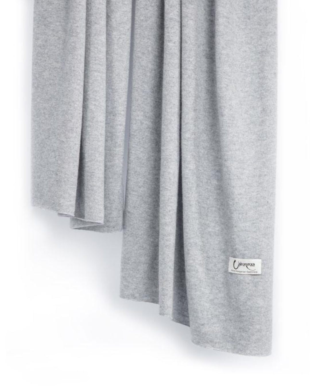Det store tætstrikkede cashmere tørklæde i lys grå hænger løst.