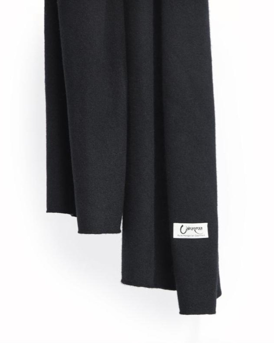 Det store tætstrikkede cashmere tørklæde i sort hænger løst.