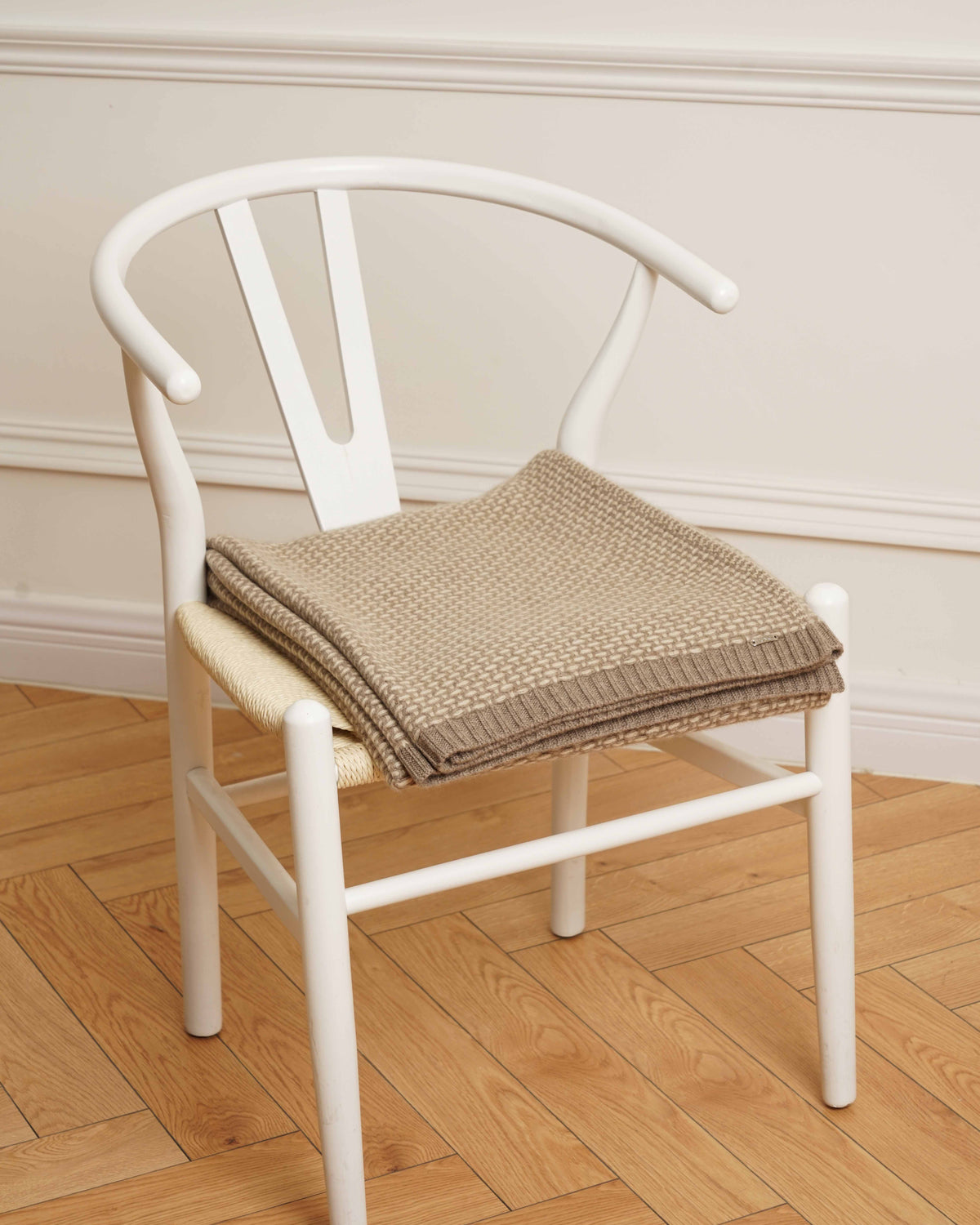 Taiga cashmere plaid i natural taupe og natural sand, foldet på en hvid stol.