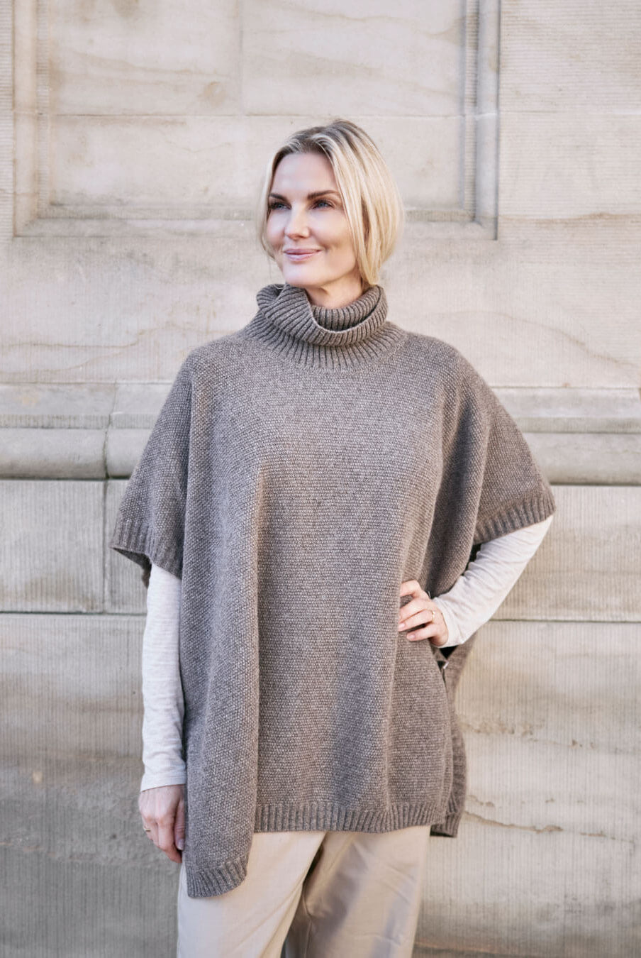 Model bærer Tara yakuld poncho med rullekrave i Yak Dark Grey.