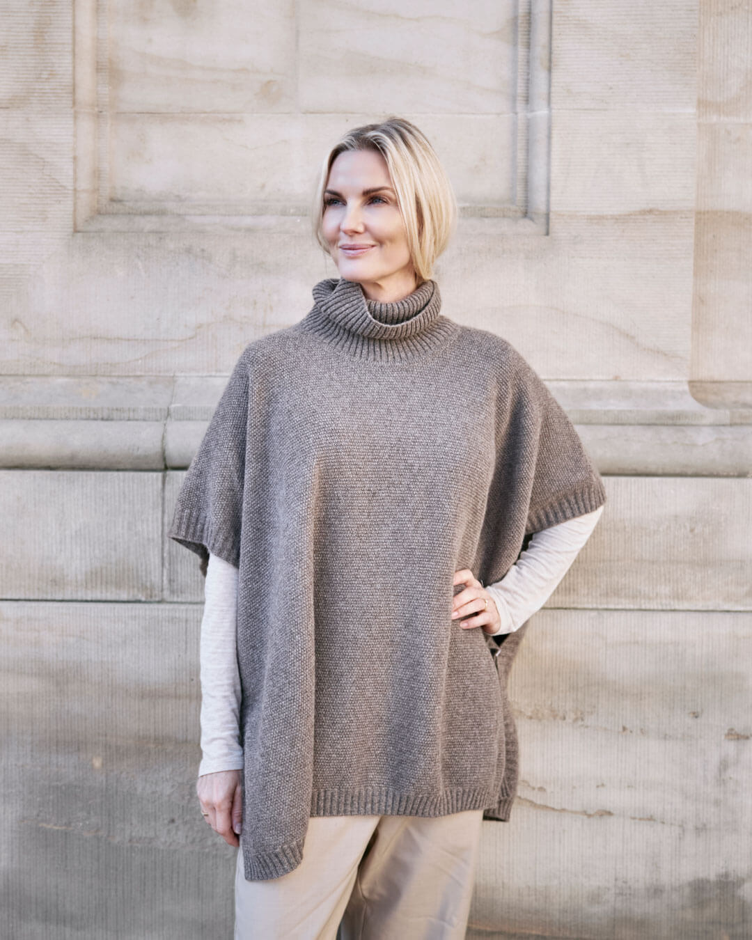 Model bærer Tara yakuld poncho med rullekrave i Yak Dark Grey.