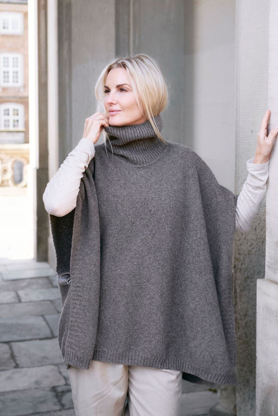Model ved portal iført Tara yakuld poncho med rullekrave.