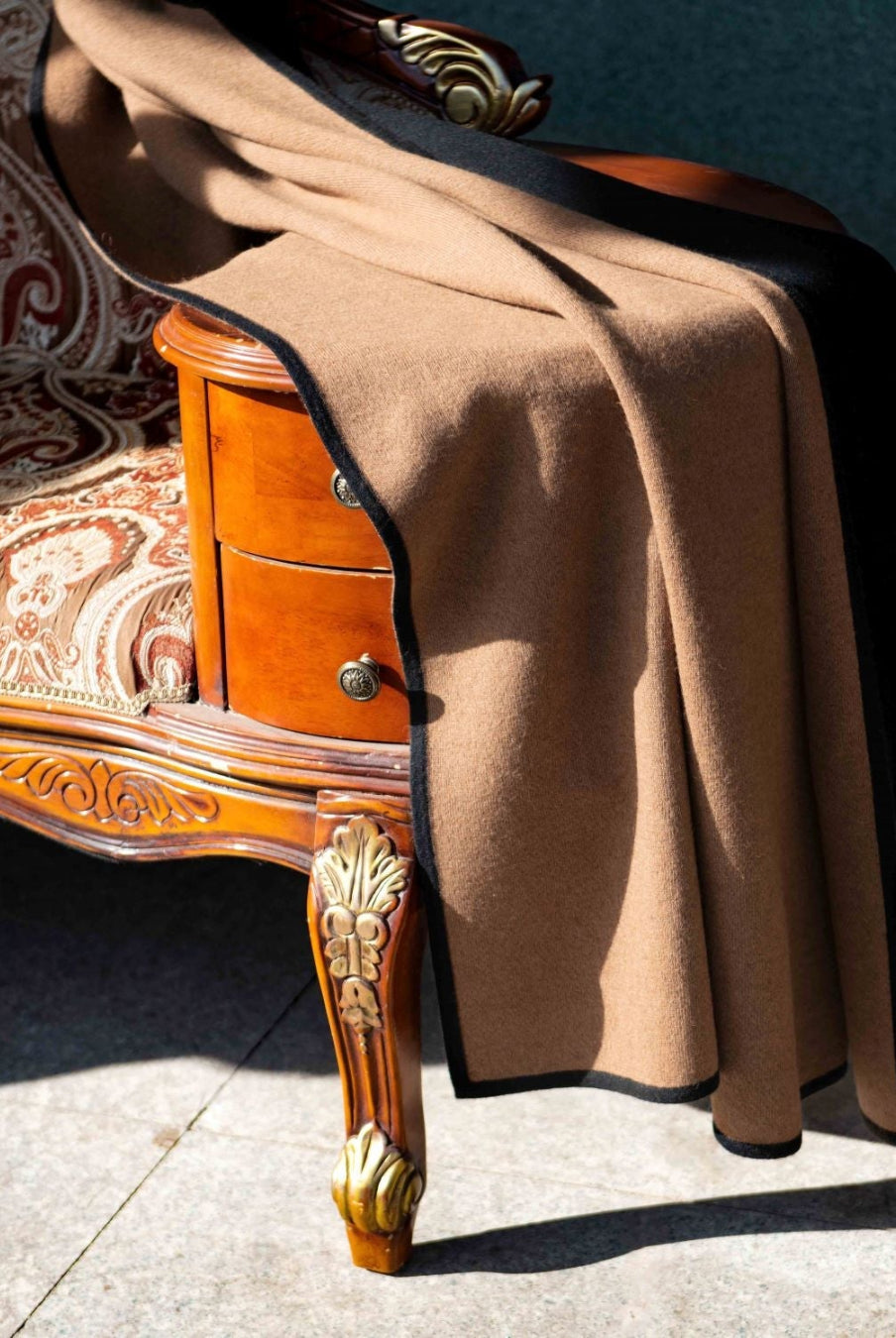 Plaid draperet over en sofa, der viser siden med den naturlige brune kameluldfarve, samtidig med, at man ser en kant af den sorte yakuld.