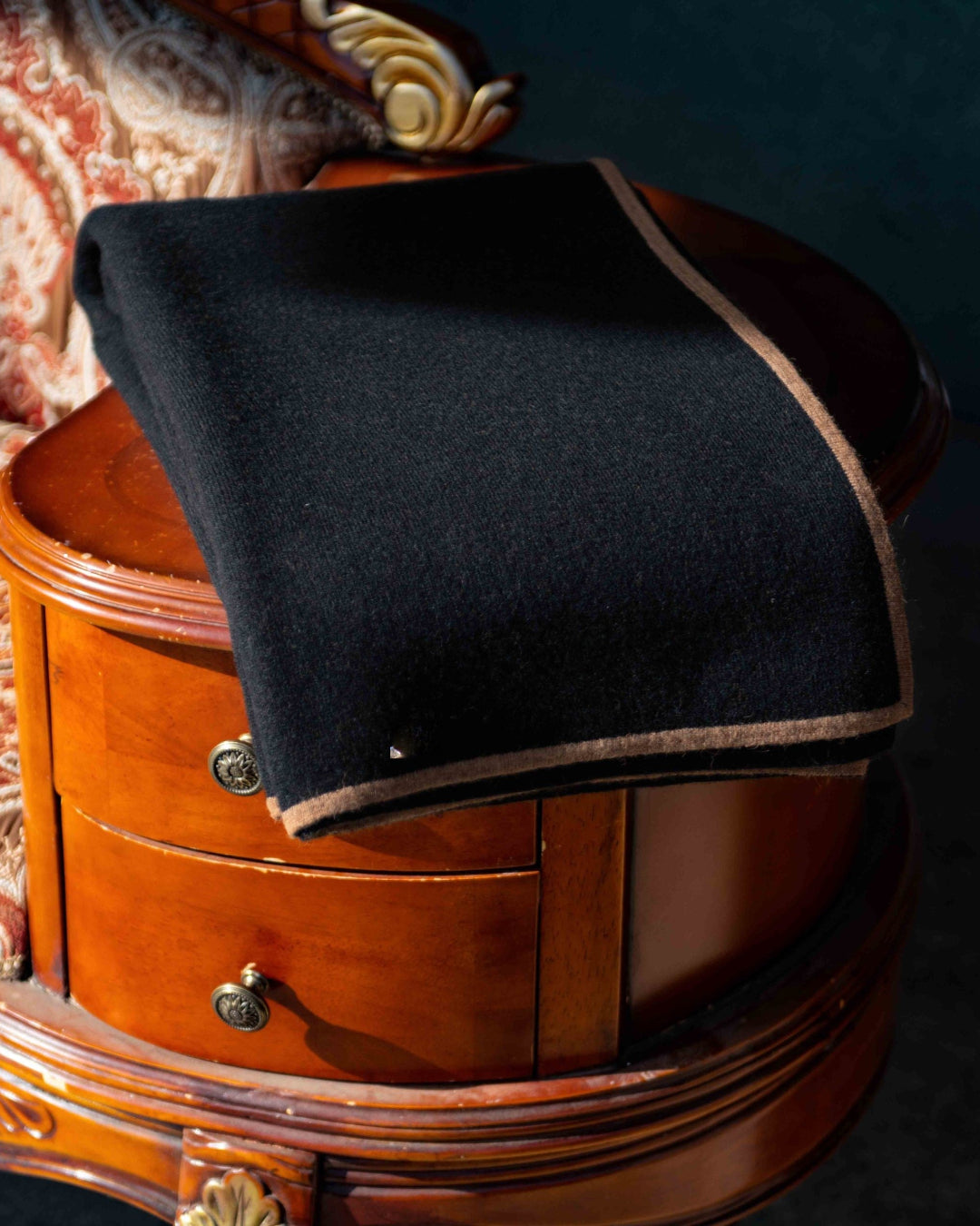 Yak- og kameluldsplaid liggende foldet på kanten af en klassisk sofa med den sorte side udad, mens man ser en streg af den brune kameluld.