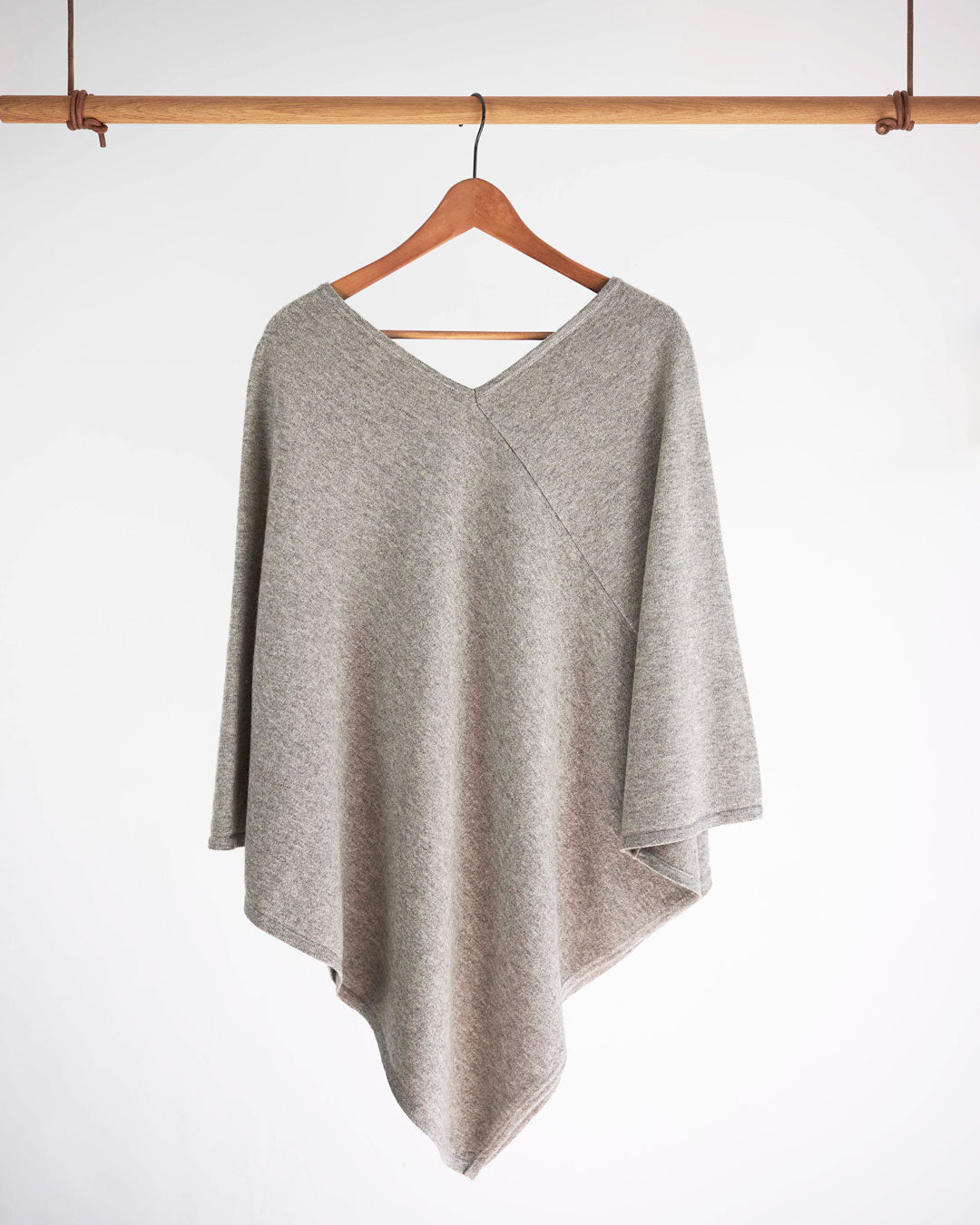 Poncho i yakuld, platinum grey, hængende på bøjle mod hvid baggrund.
