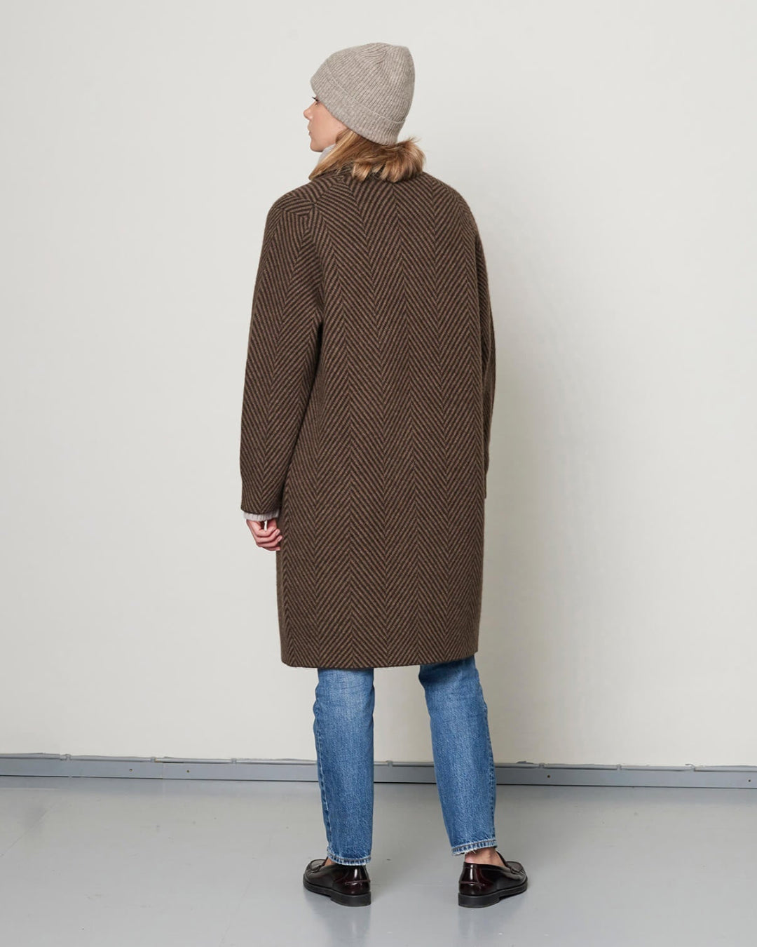 Modellen med yakuld frakken set bagfra, hvilket fremhæver det elegante fald og det smukke sildebensmønster.