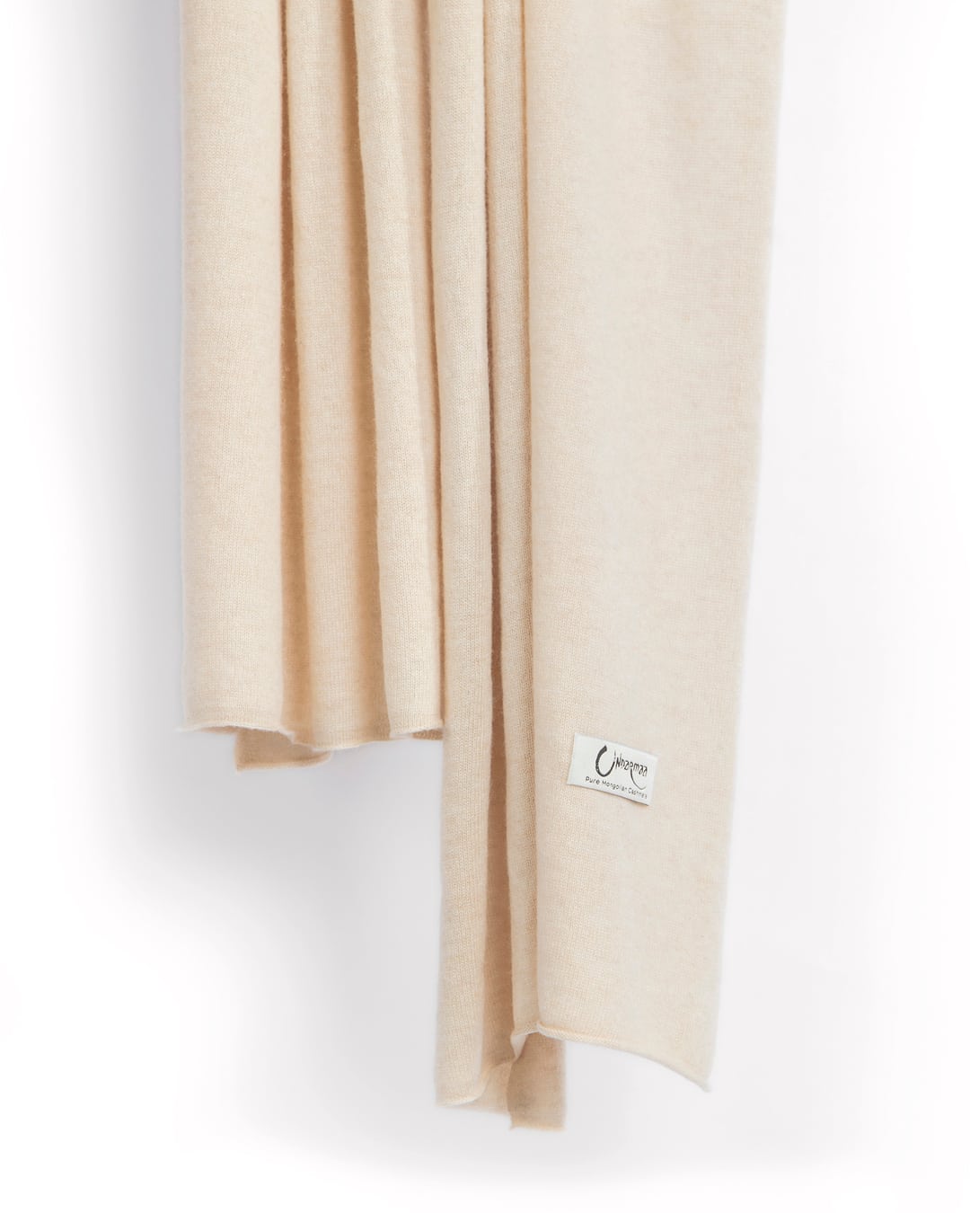 Det store cashmere tørklæde, her i naturfarvet lys beige hænger løst ned.