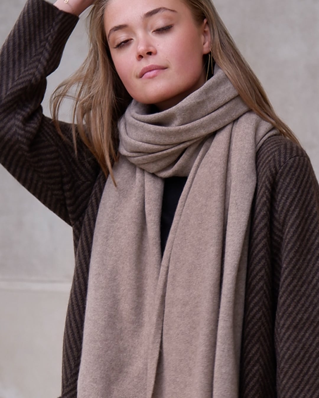 Model med det store naturfarvede cashmere tørklæde i mørk gråbeige, draperet løst om skuldrene.