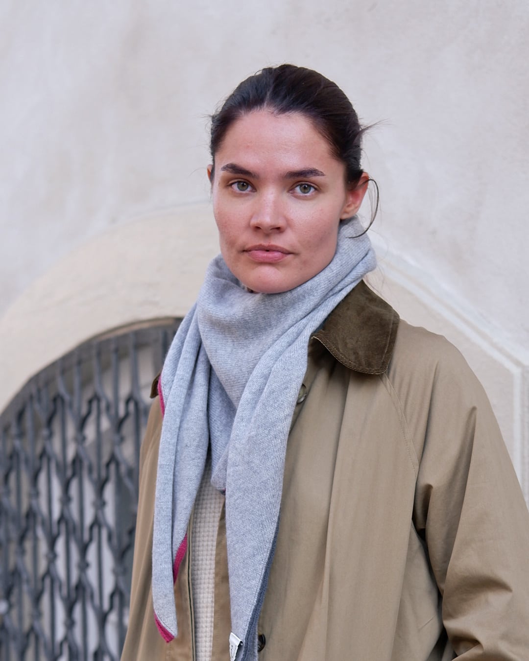 Model med Zul trekantet tørklæde i lysegrå, båret over en trenchcoat.