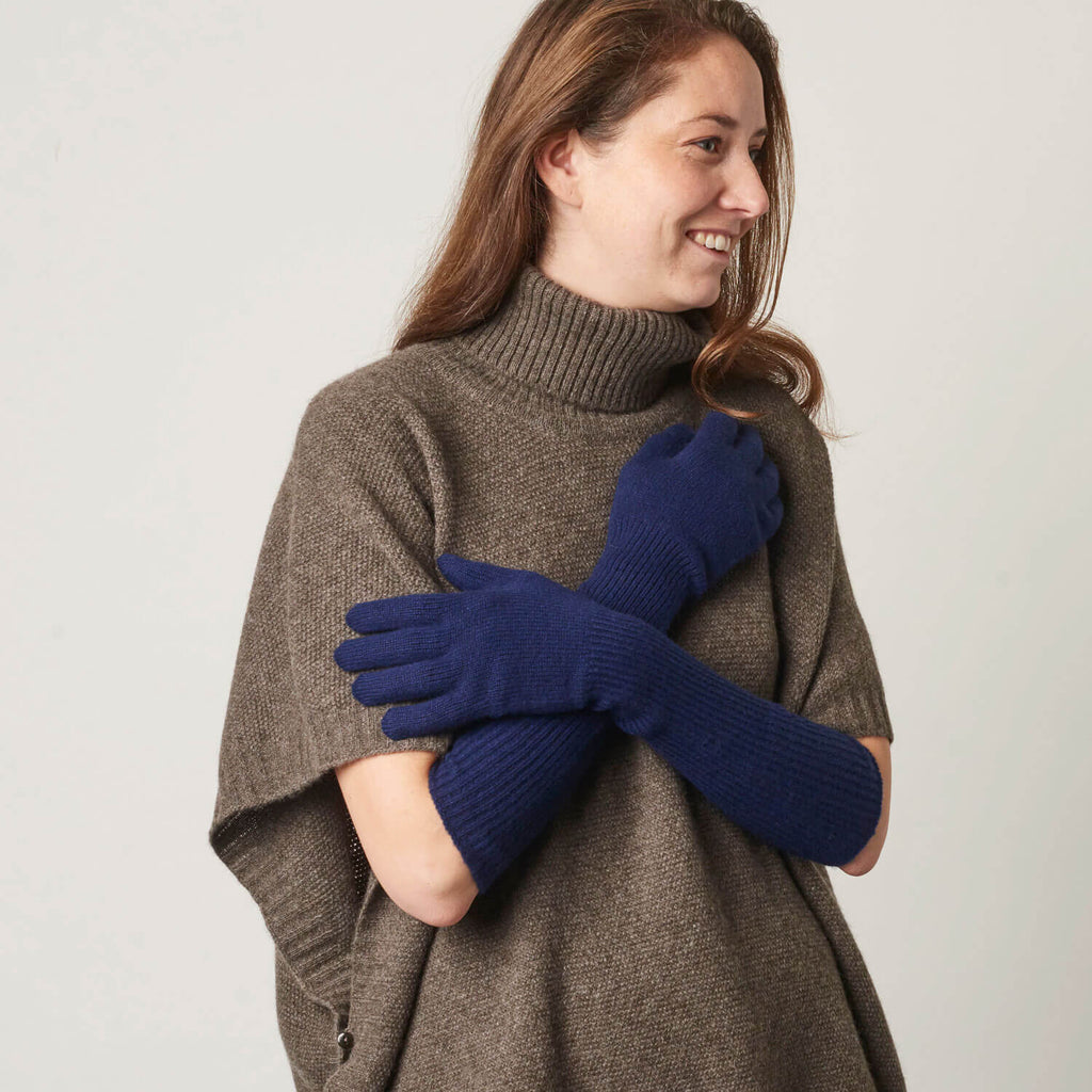 Model præsenterer lange cashmere handsker i en marineblå farve.
