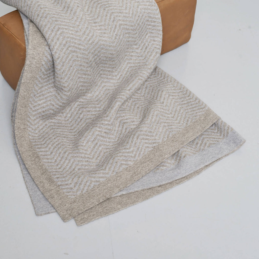 Cashmere og yakuld plaid draperet over en puf, så man kan kombinationen af naturliggrå og lyseblå, og plaidens tekstur.