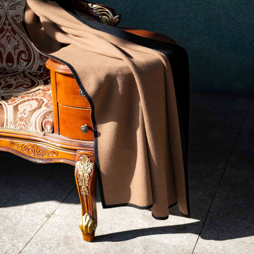Plaid draperet over en sofa, der viser siden med den naturlige brune kameluldfarve, samtidig med, at man ser en kant af den sorte yakuld.
