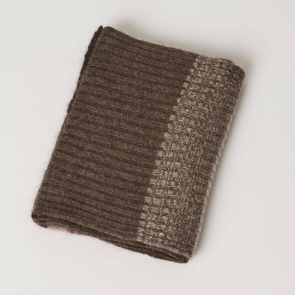 Stilfuldt billede af yakuld halstørklædet foldet pænt, der viser farvekombinationen, primært den brune farve.