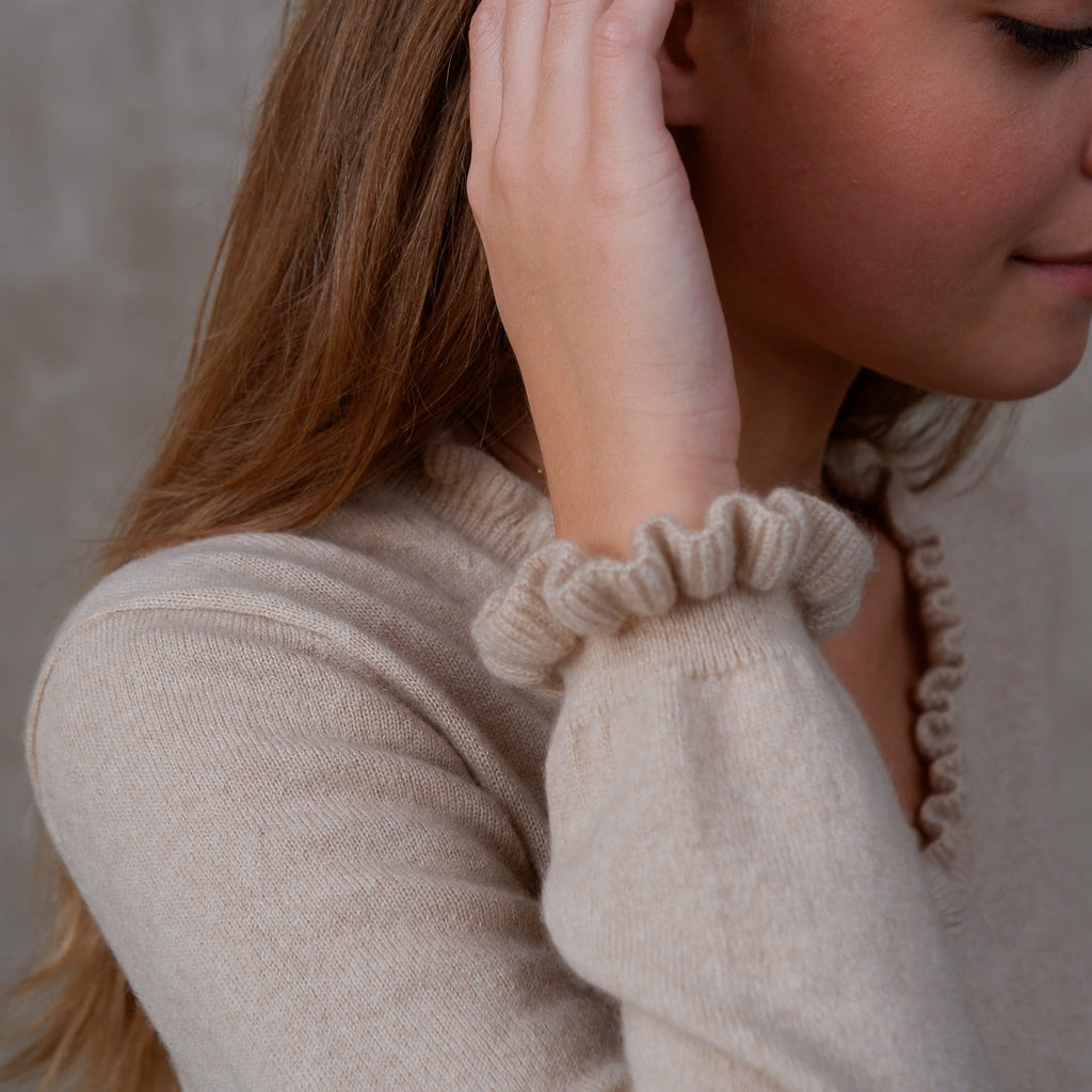Model iført cashmere bluse i Natural Sand med flæsedetaljer ved halsudskæring.