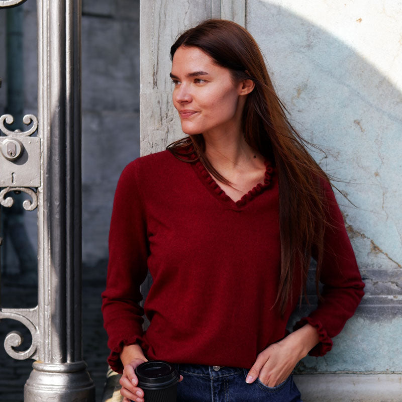 Kvinde iført cashmere bluse i Pinotrød med flæsedetaljer ved halsudskæring.