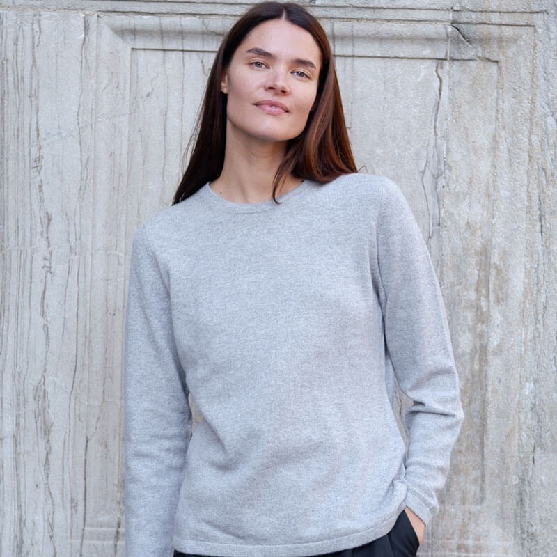 model iført rund hals cashmere crewneck i lys grå foran en mur. 