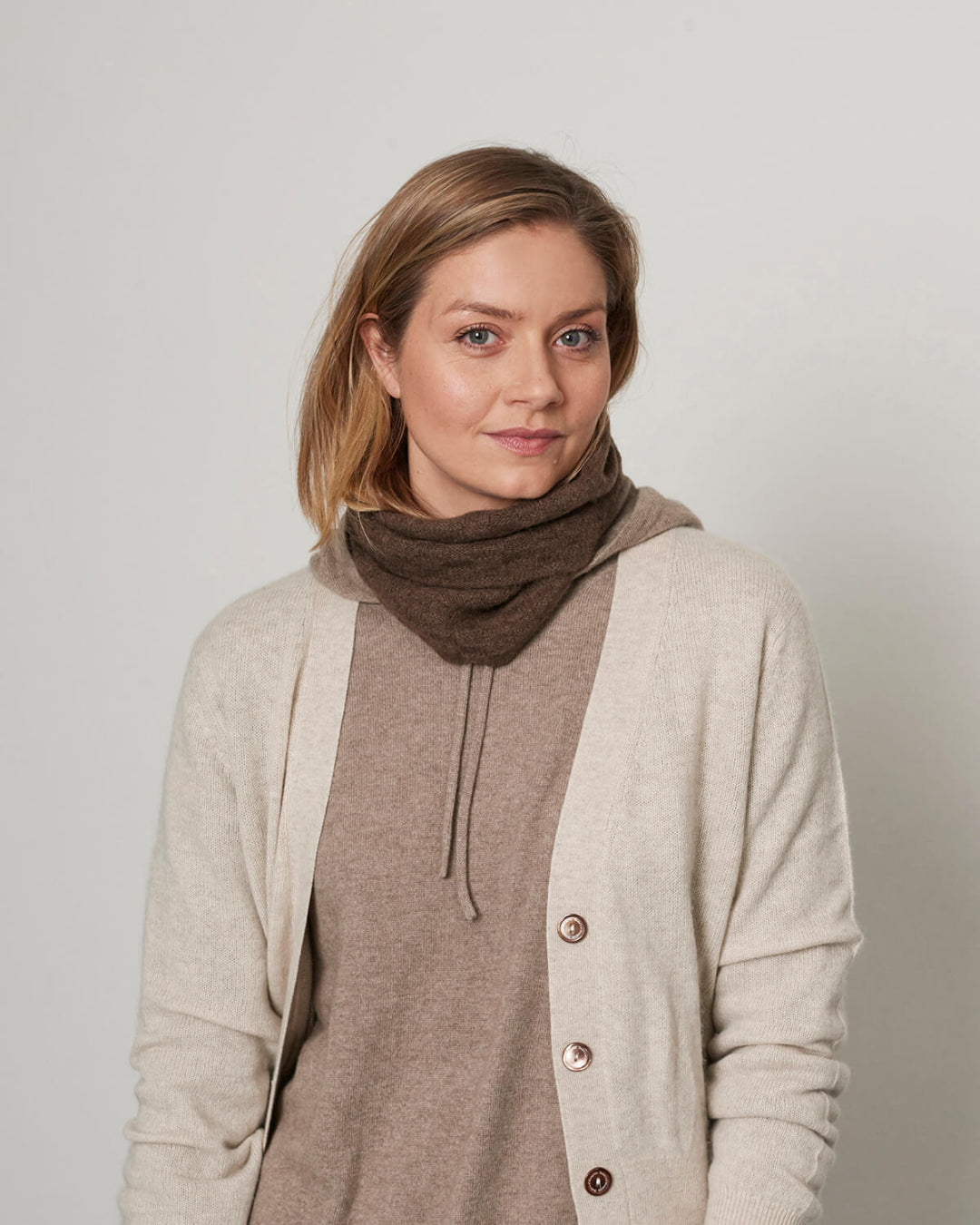 Model iført lys camel cashmere cardigan med V-udskæring, parret med en halsedisse.
