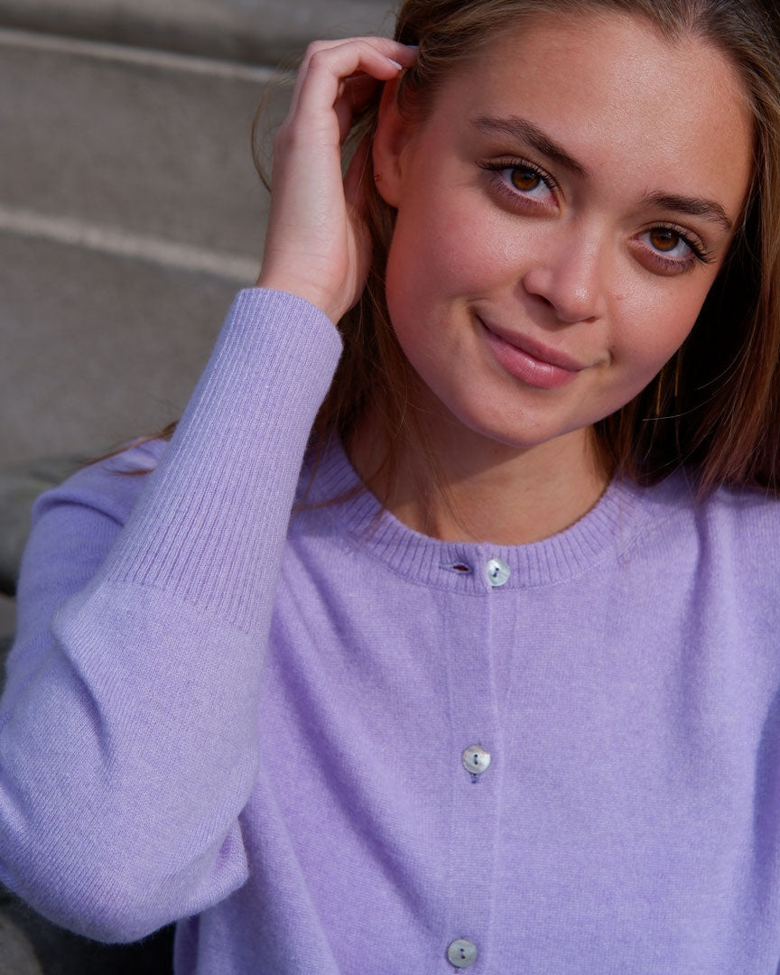 Smilende kvinde iført lavendel cashmere cardigan med knapper, sidder på en trappe.
