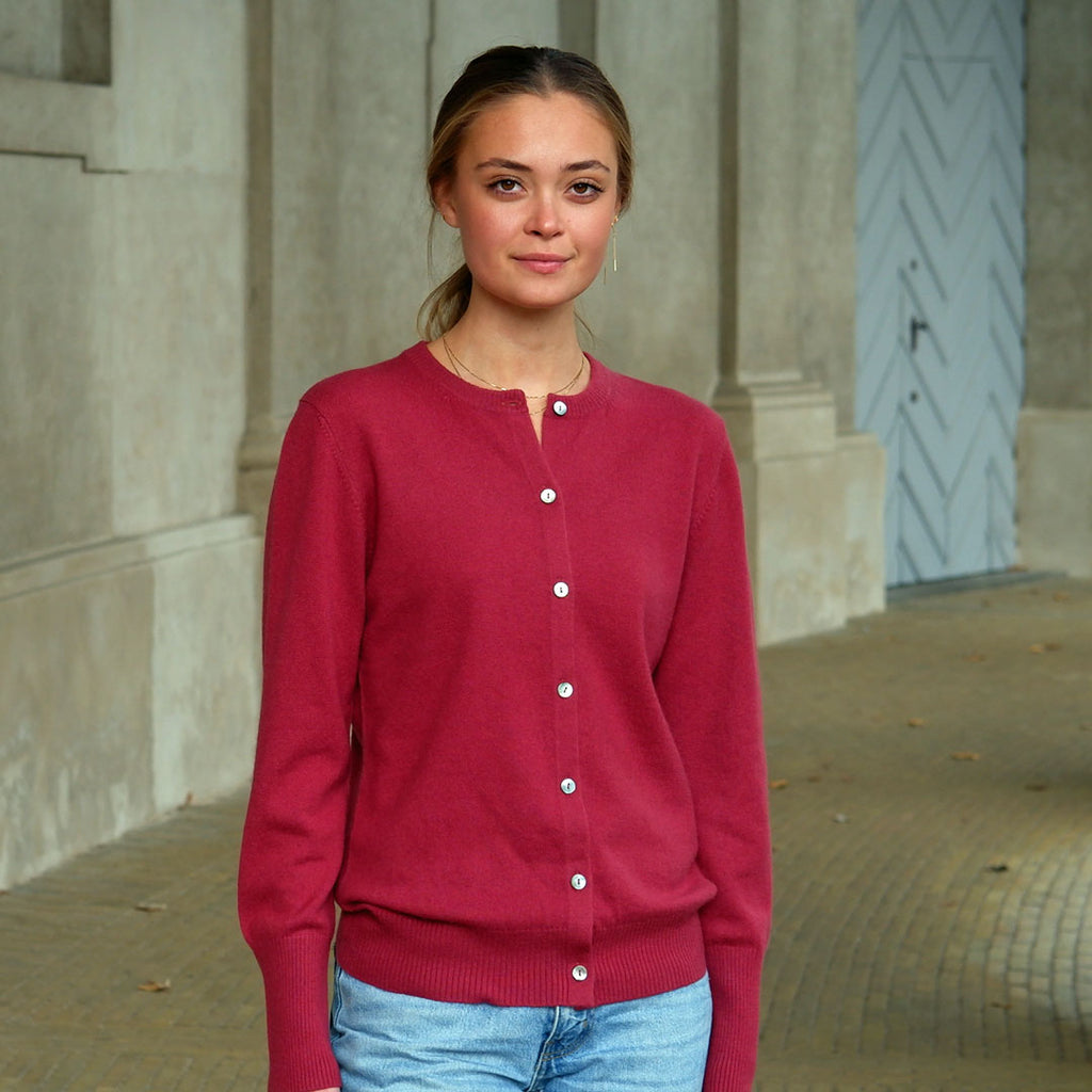 Kvinde iført en Pinot Red cashmere cardigan med knapper, står foran en søjlegang.