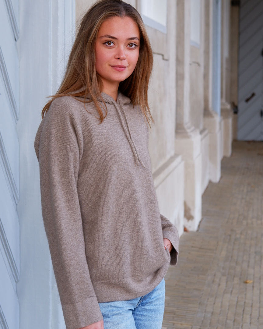 Model i taupe beige cashmere hoodie foran klassisk bygning