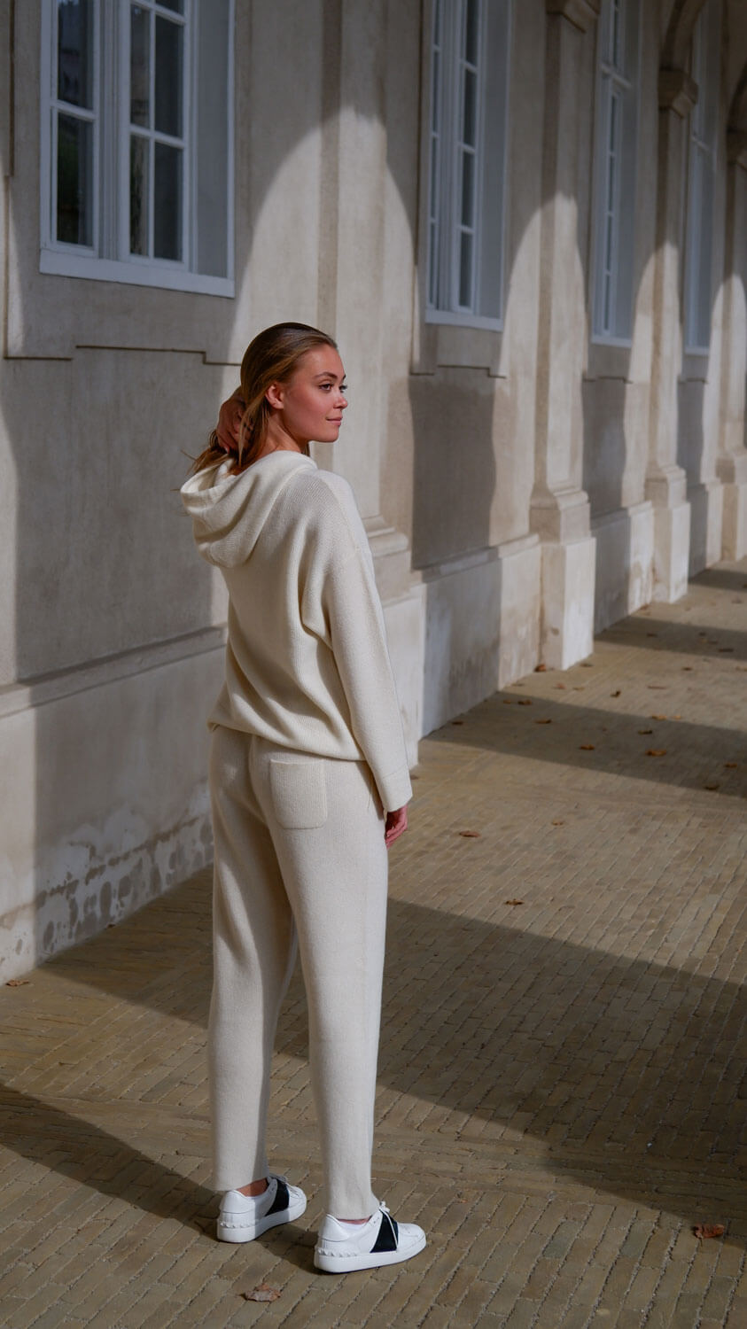 Model iført hvid cashmere hoodie og cashmere bukser som sæt, set bagfra, så man se buksernes lommer.