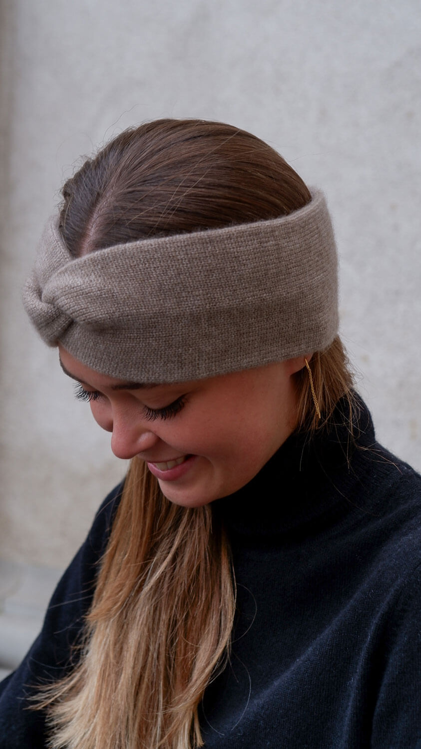 Model iført mørk gråbeige pandebånd (ørevarmer) set fra siden. 