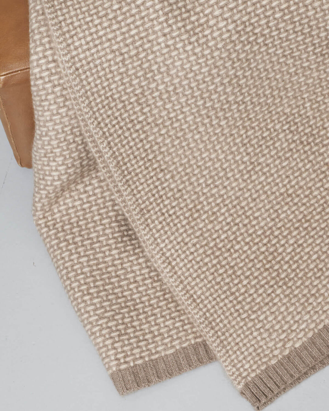 Nærbillede af cashmere plaidens fine strikmønster i lyse og mørke beige toner.
