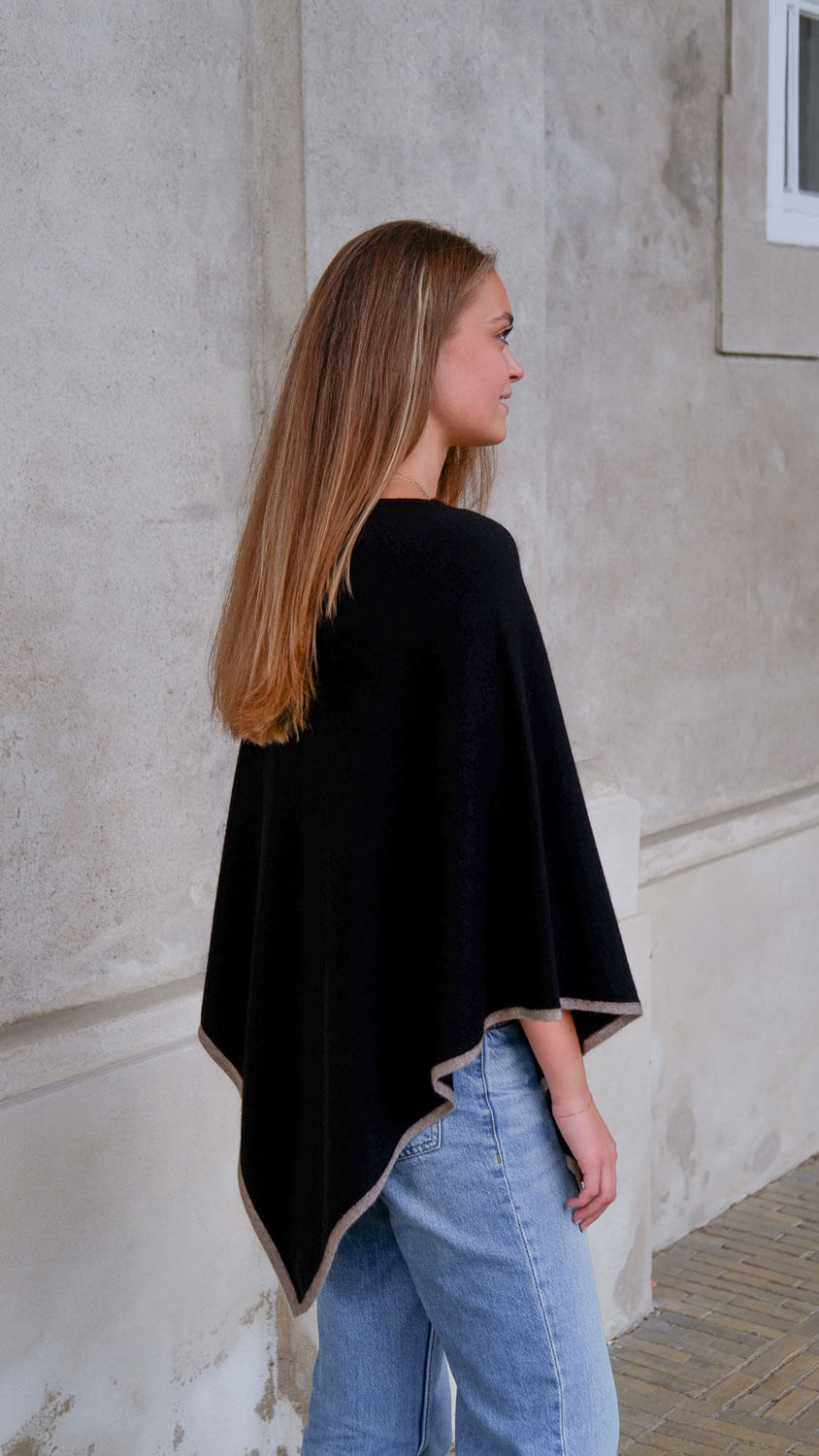 Model iført sort cashmere poncho med mørkbeige kant.