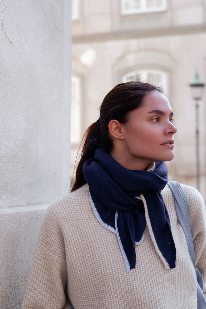 Cobalt-blåt cashmere tørklæde med lyseblå og beige kanter, smukt foldet omkring halsen.