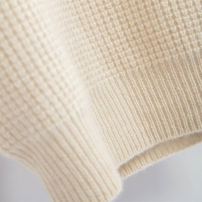 Closeup af cashmere lys beige turtleneck, der viser den fine ternede struktur i strikken.