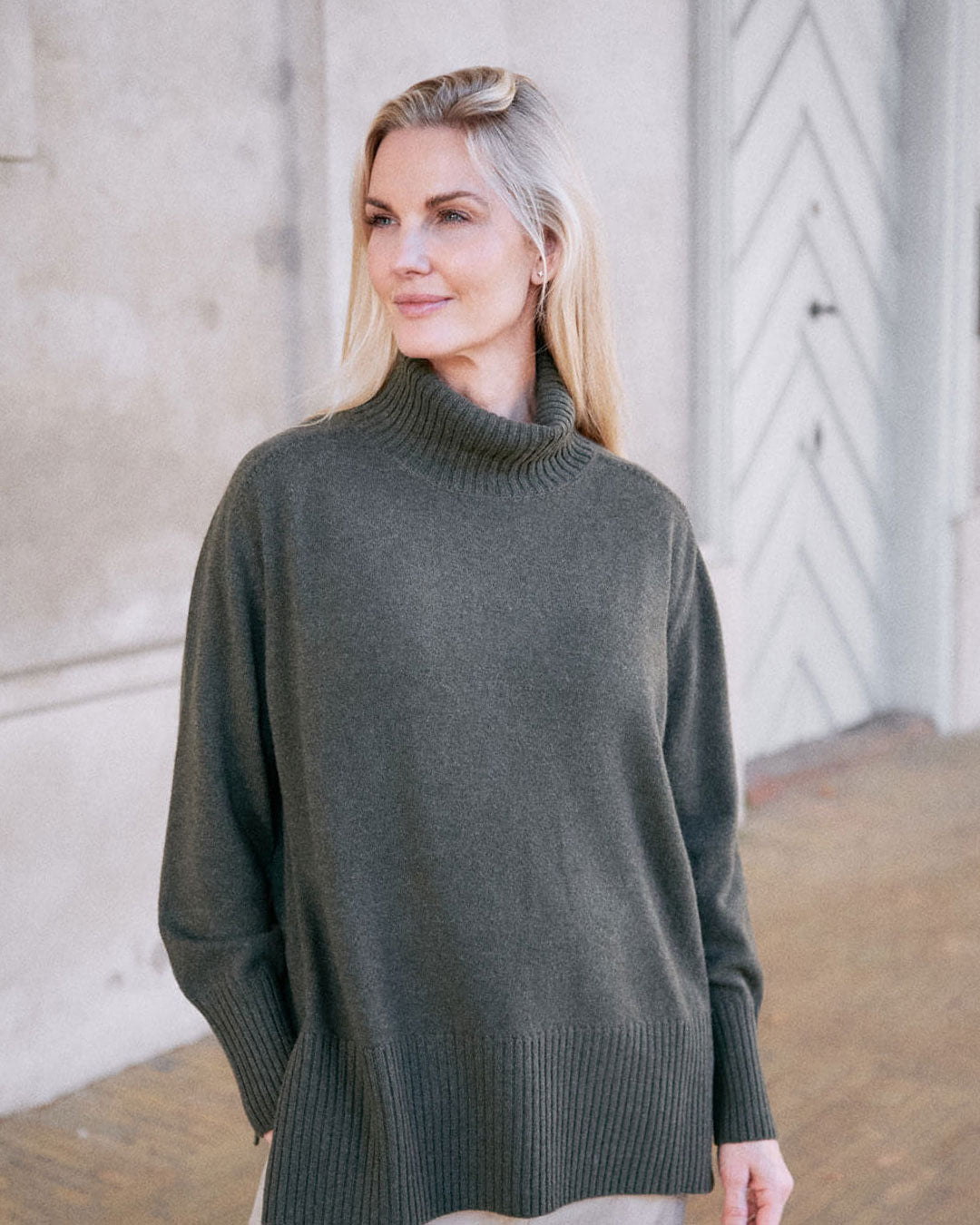 Model iført klassisk cashmere sweater med sadelskuldre og løs pasform i army green i afslappet pose.