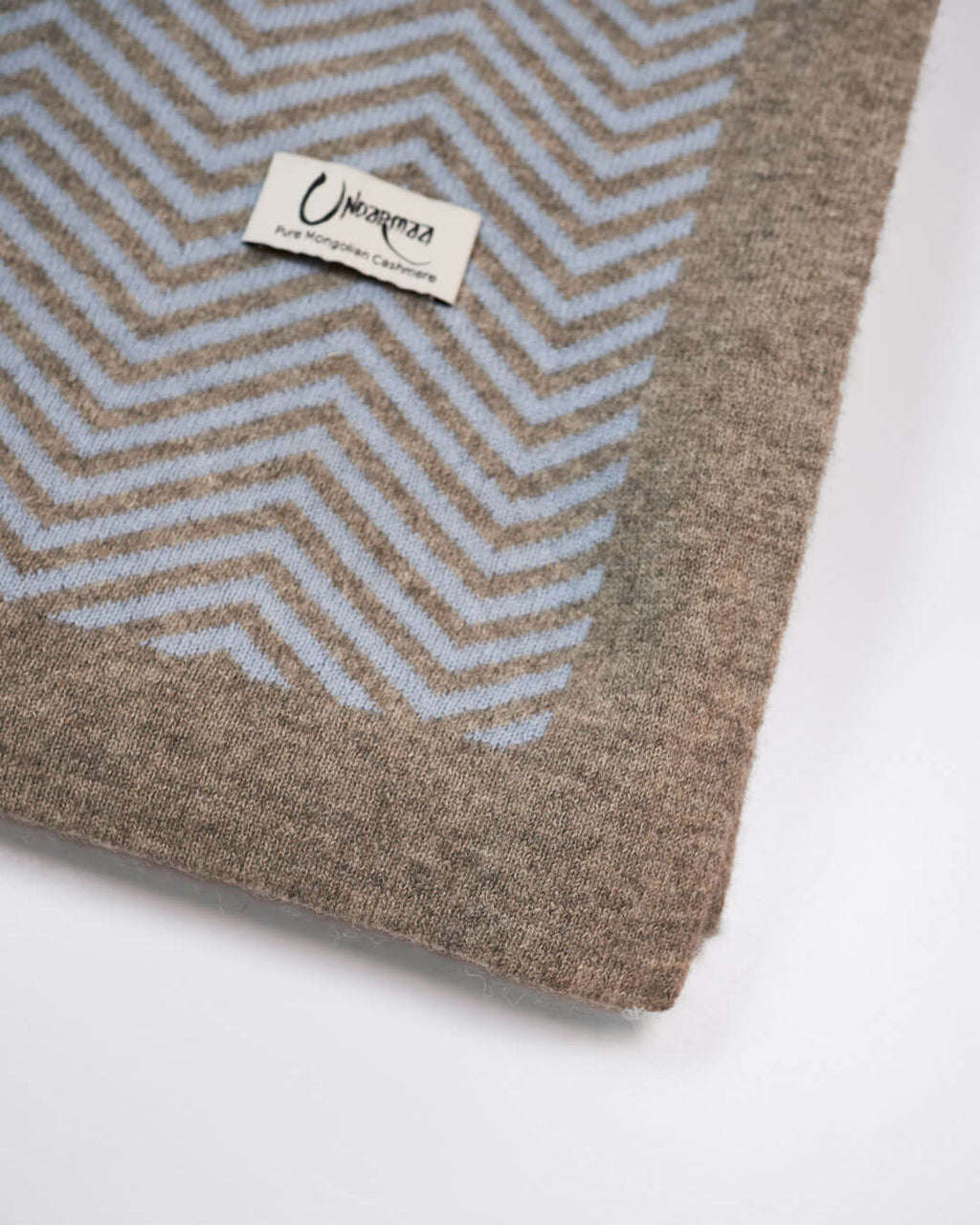 Detalje af plaid i ice blue cashmere og platinum grey yakuld med Undarmaa-logo, i sildemønstret design.