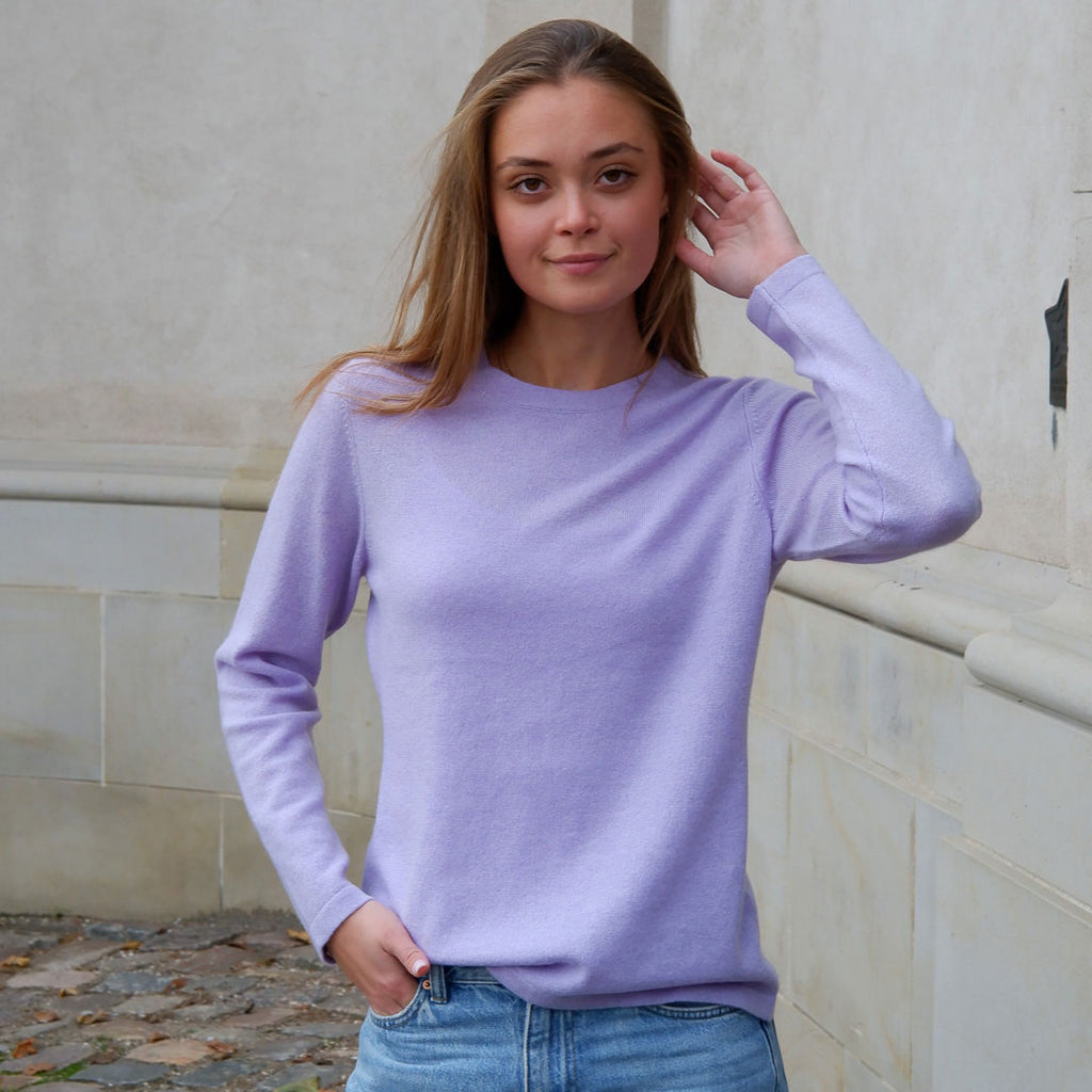 Kvinde iført en lavendel farvet cashmere crewneck med rund hals, stående foran en lys mur.