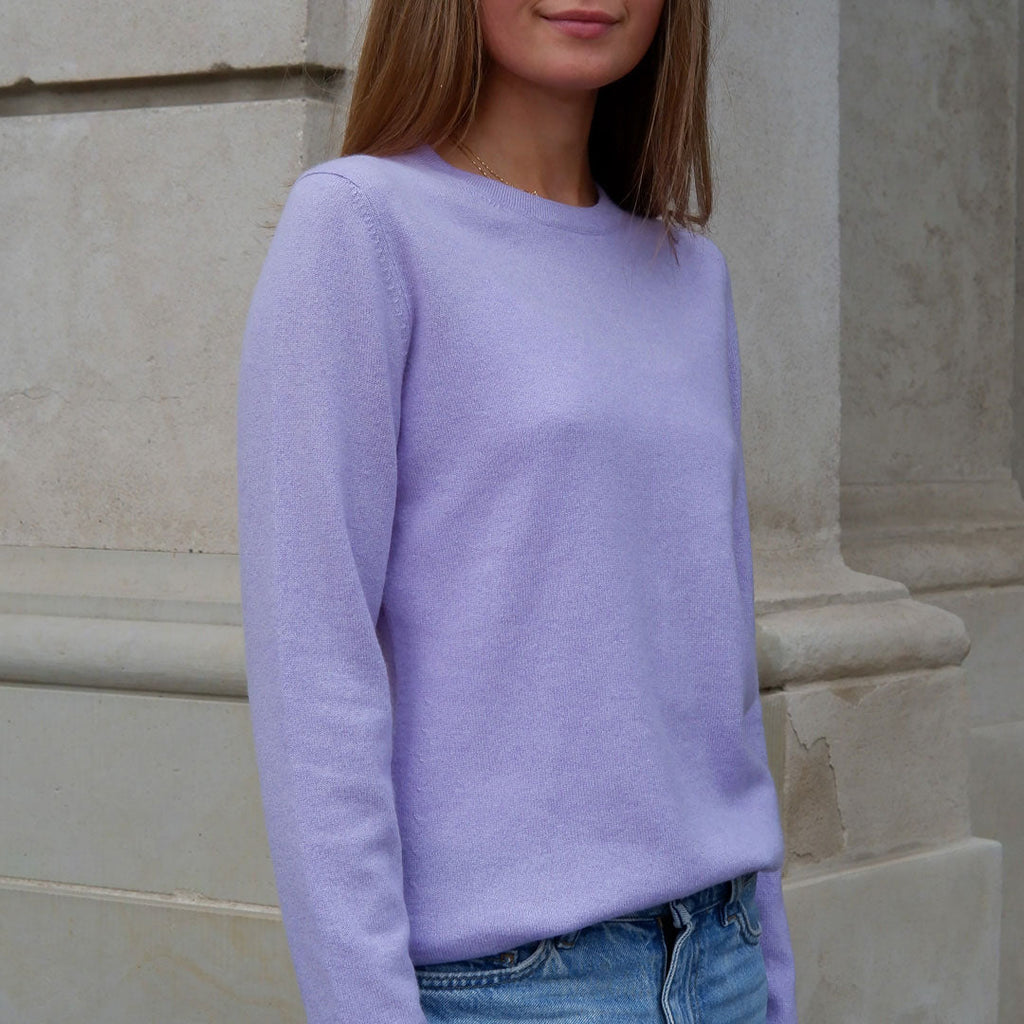 Kvinde i en lavendel farvet cashmere bluse med rund hals, fotograferet tæt på foran en søjle.