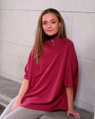 Kvinde siddende i cashmere poncho Enkh i Raspberry, viser faldet i strikket.