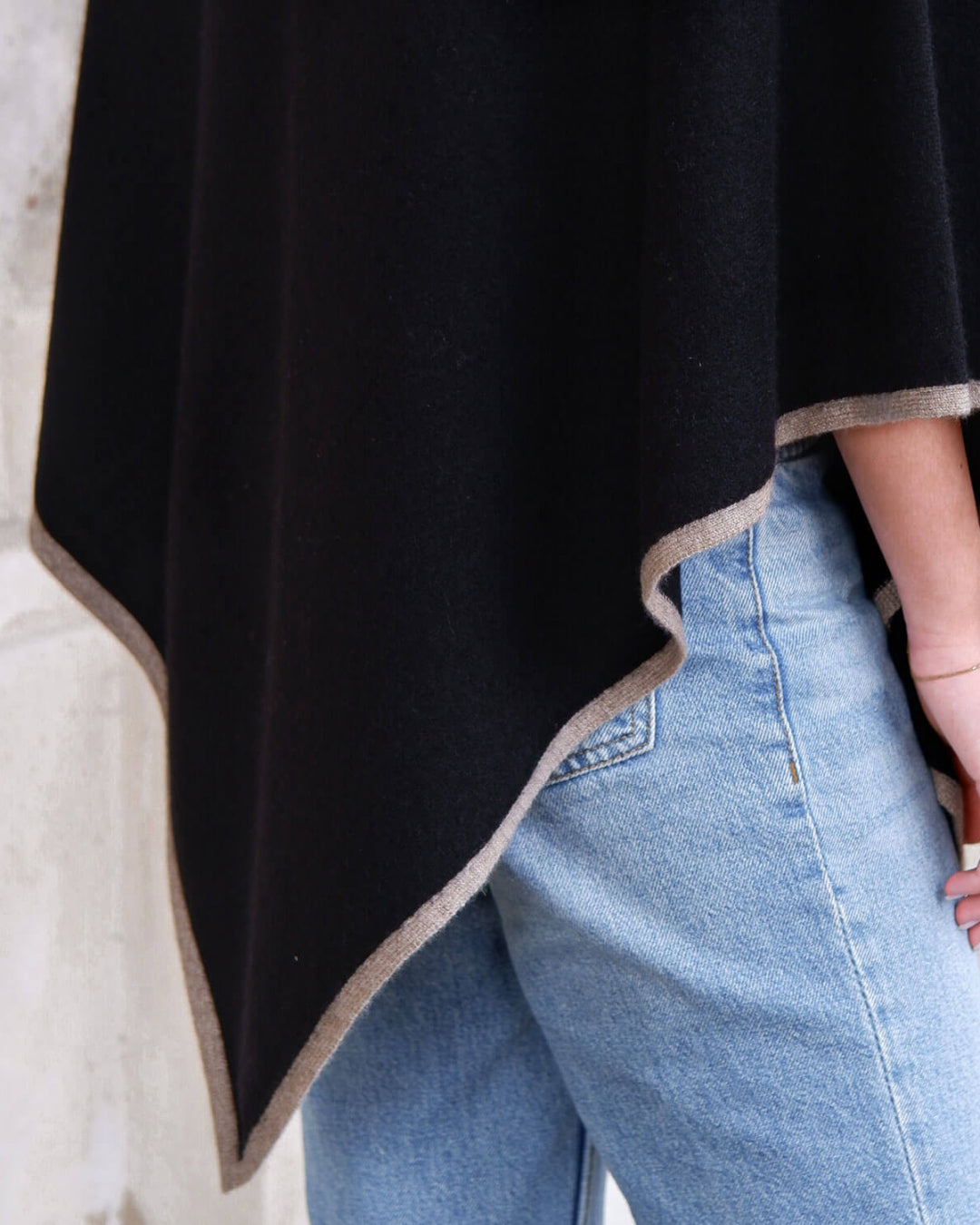 Nærbillede af sort cashmere poncho med stribet kant.